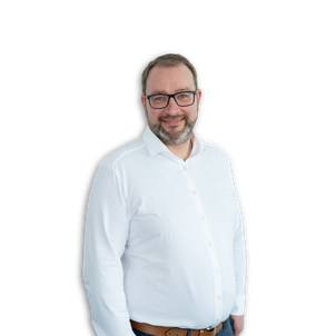 Ein Mann mit Brille, Bart und kurzen Haaren, der ein weißes Hemd und Jeans trägt, steht vor einem schlichten weißen Hintergrund und lächelt in die Kamera.